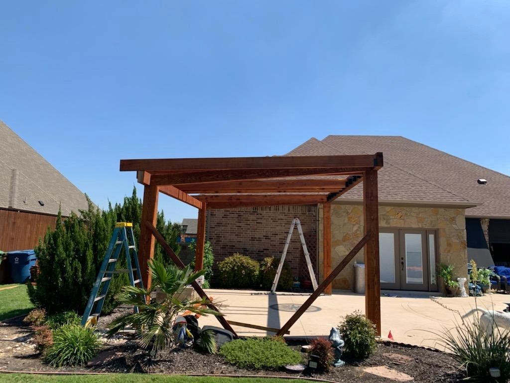 Cedar pergola framing going up on a stone patio behind a brick home