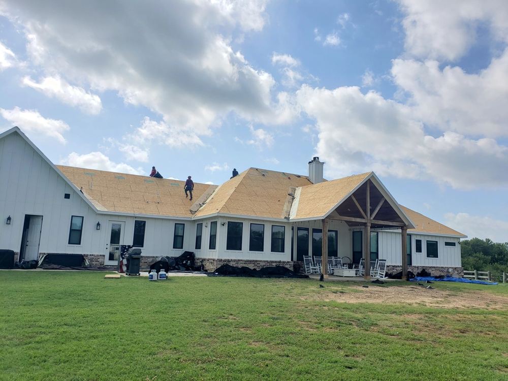 Wide view of a large home mid-roof-replacement with workers on the ridge